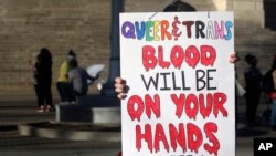 FILE - A protester outside the Kansas Statehouse holds a sign after a rally for transgender rights on the Transgender Day of Visibility, March 31, 2023, in Topeka, Kan.