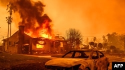 The carcass of a burnt-out car is seen as home burns during the Eaton fire in the Altadena area of Los Angeles county, California on January 8, 2025.