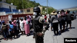 A Haitian National Police (PNH) officer looks on as Haitians stand behind him in the in the border of Malpasse, Haiti, March 17, 2020. 