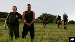 FILE - An unidentified Dominican migrant is escorted by a Border Patrol officer after being detained by Puerto Rico police near La Esperanza beach in the northern coastal town of Manati, Puerto Rico, Oct. 8, 2007.